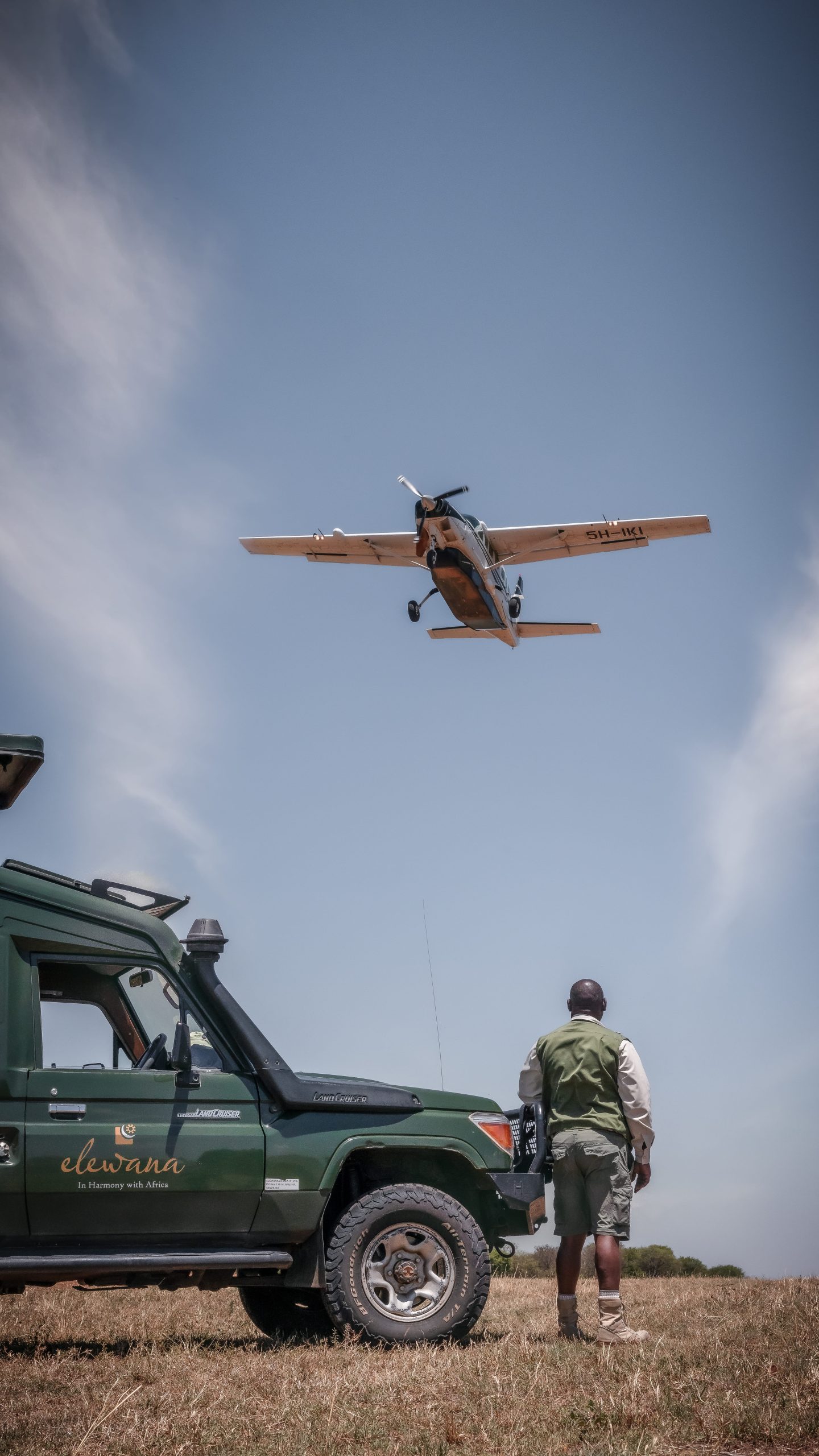 A light aircraft above a parked safari vehicle, tall crop