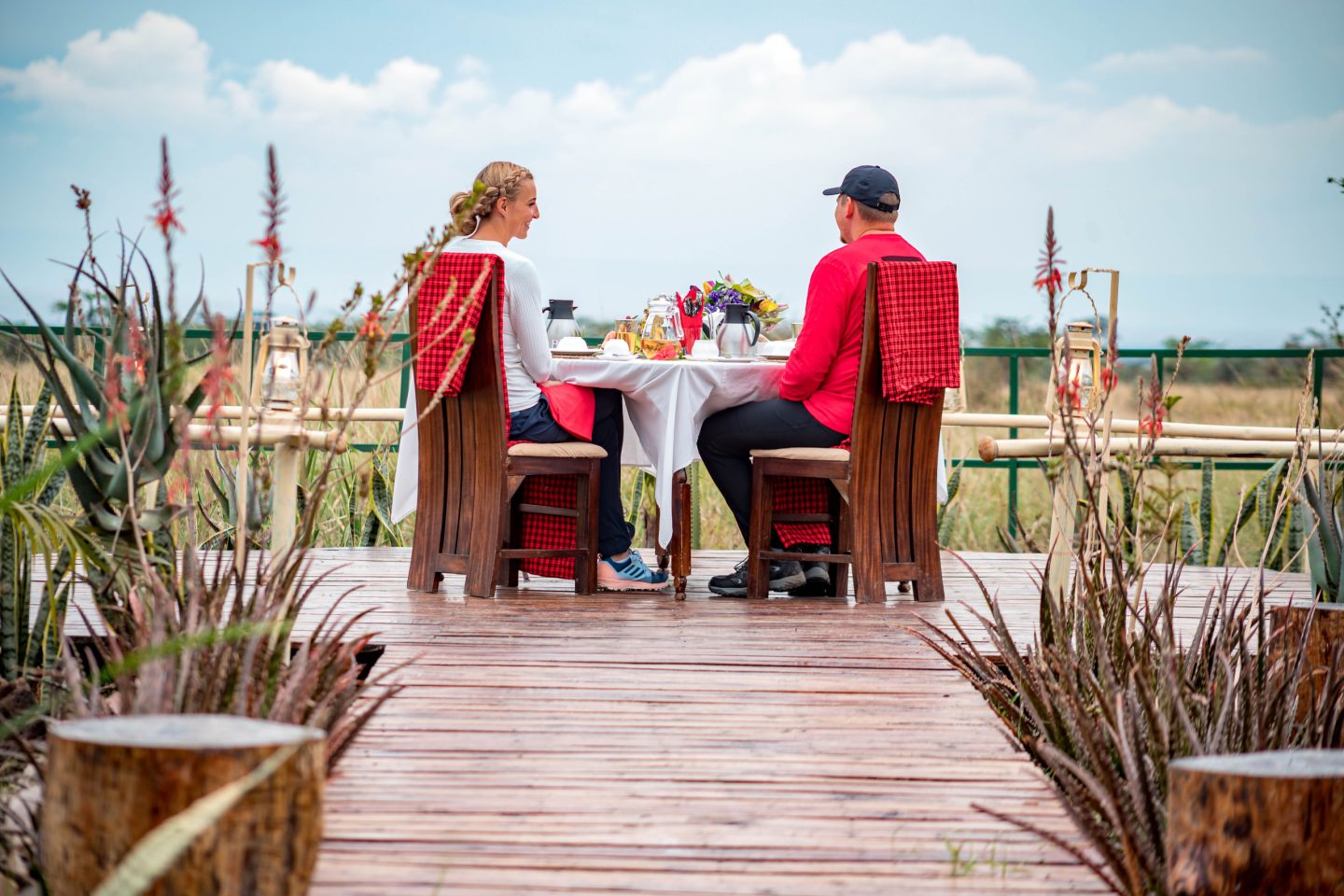 A couple dining on a raised deck, attended by staff in red