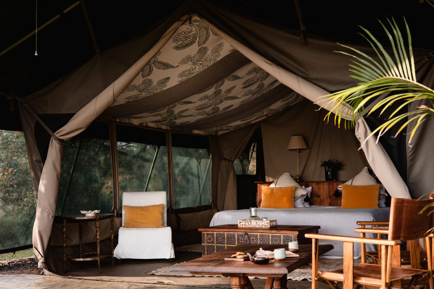 A canopied bed inside a safari tent, lamps lit either side